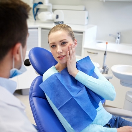 Woman in dental chair holding her cheek in pain